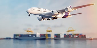 Airplane in the foreground flies over the harbour and ships can be seen in the background.