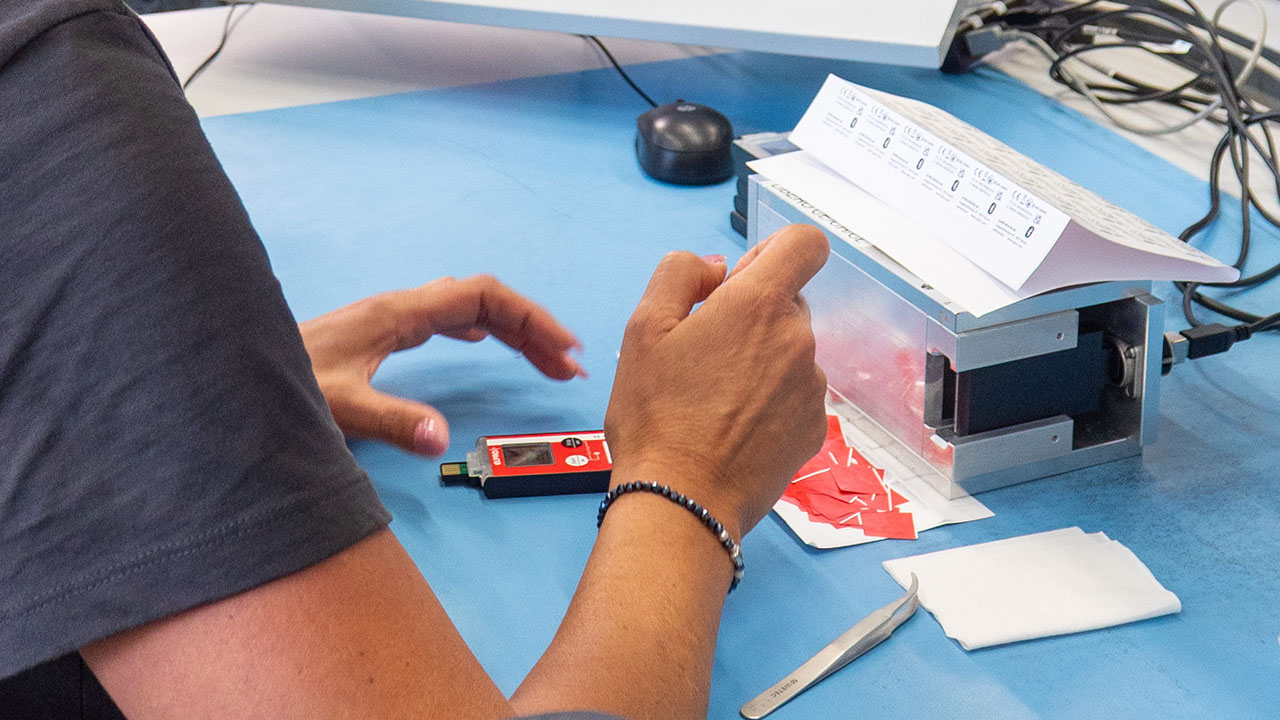 An employee's fingers are sticking labels onto a device