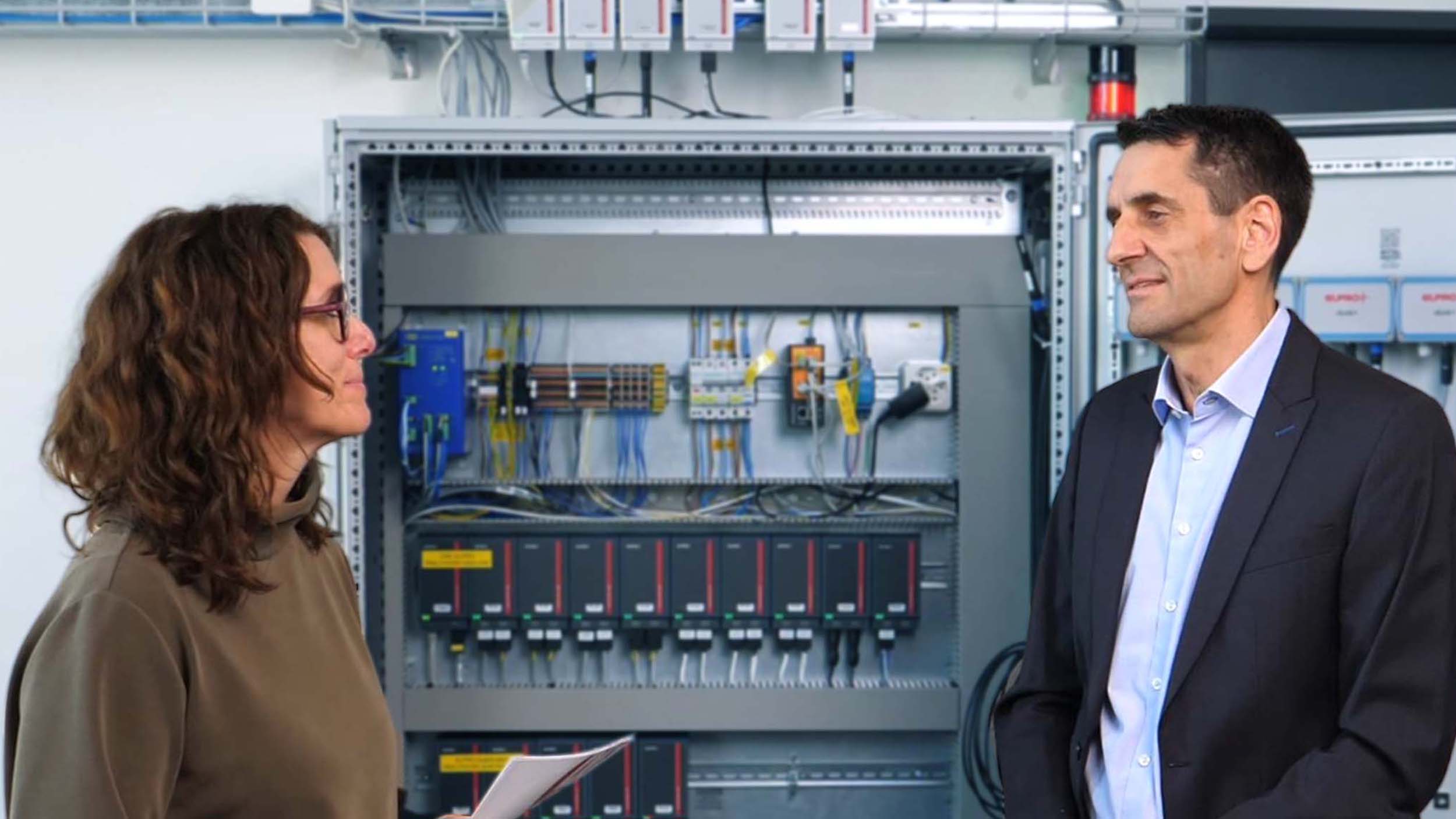 Mann spricht zu einer Frau vor einem Schaltschrank