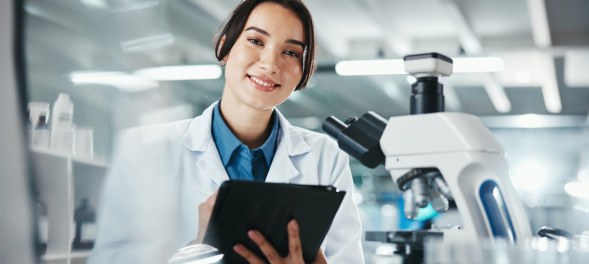 Laboratory professional using a tablet beside a microscope in a modern research laboratory, supporting clinical research, quality control, and data-driven decision-making.