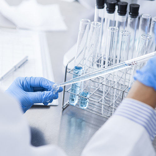 Pharmaceutical technician empties liquid into a test tube using a pipette.