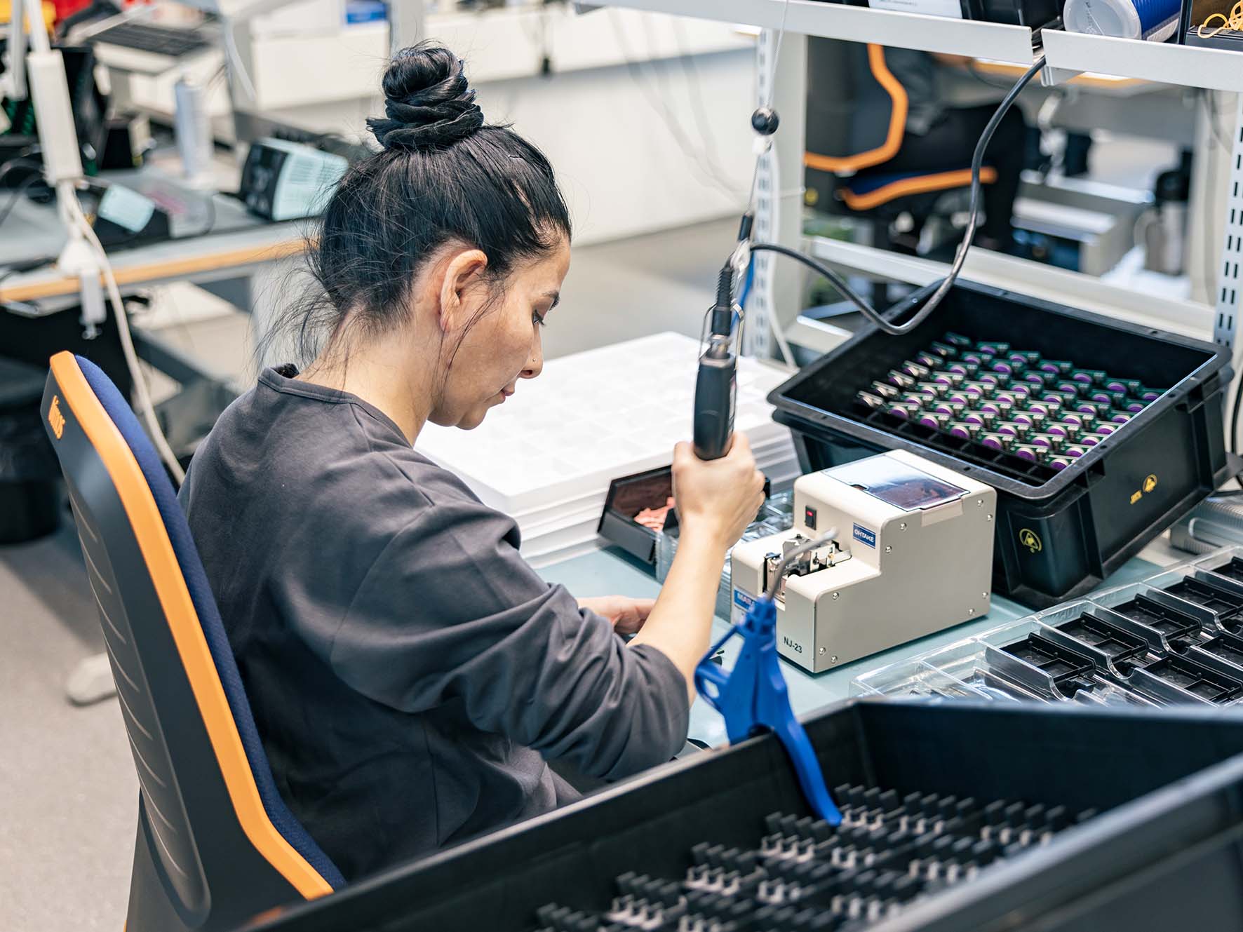 Eine Frau sitzt am Montagetisch und lötet Teile zusammen.