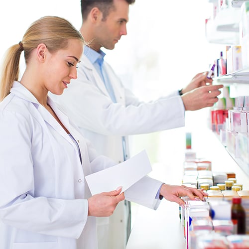 Zwei Apotheker stehen vor einem Regal mit Medikamenten in einer Apotheke.