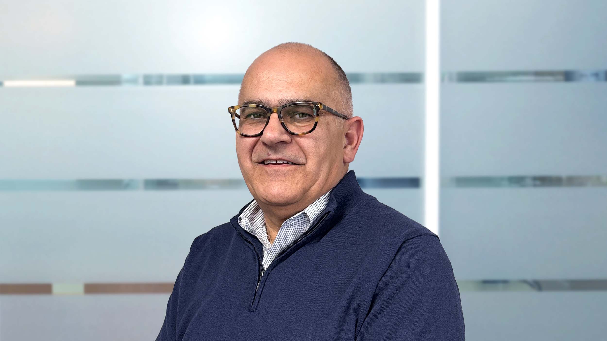 Mann schaut in die Kamera vor einer bläulichen Glaswand